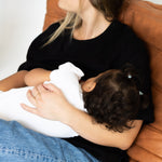 Mum feeding her baby in the black Indiana breastfeeding tee by Milky Threads Co, on a tan leather chair