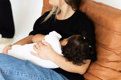 Mum feeding her baby in the black Indiana breastfeeding tee by Milky Threads Co, on a tan leather chair