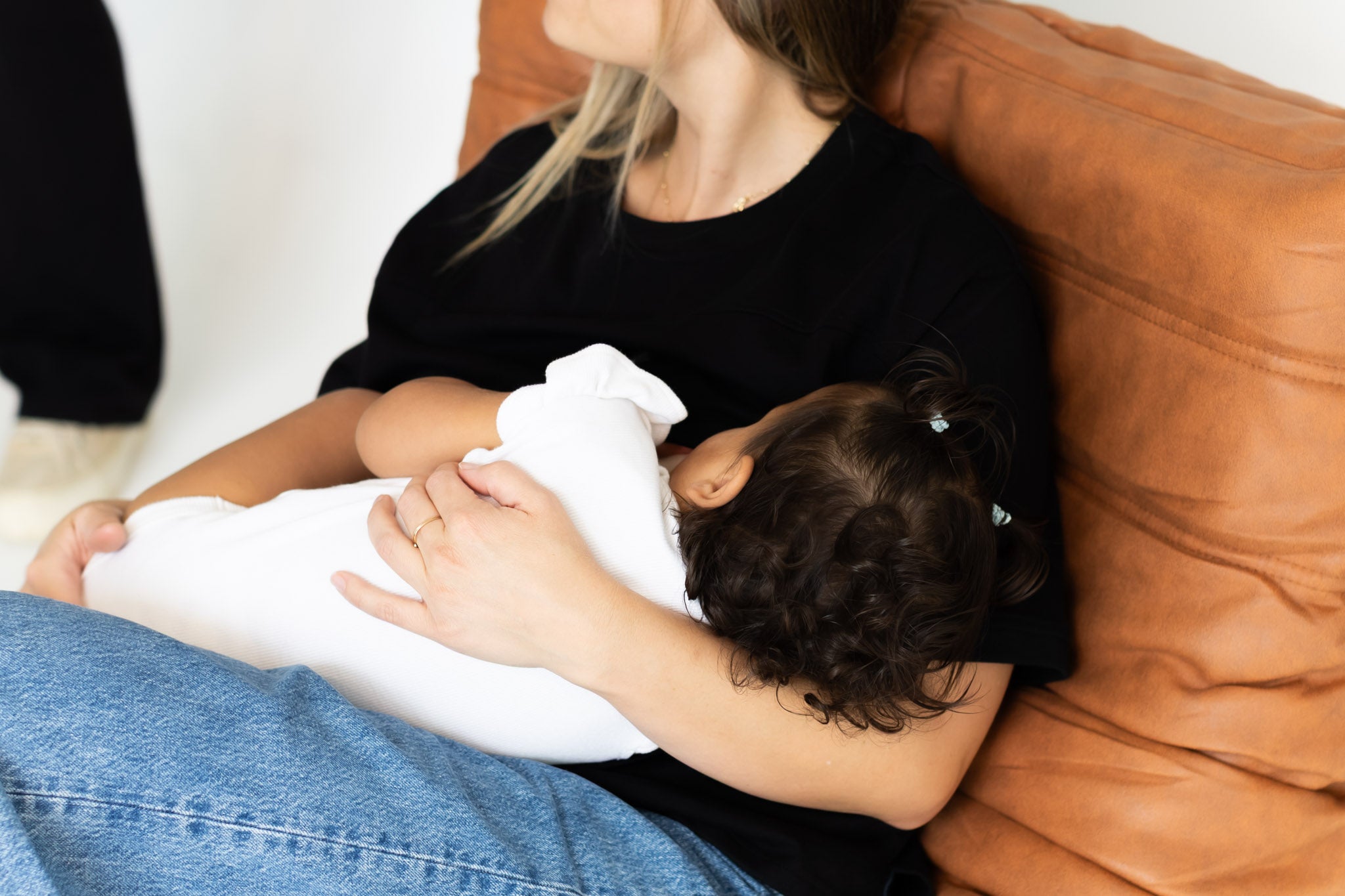 Mum feeding her baby in the black Indiana breastfeeding tee by Milky Threads Co, on a tan leather chair