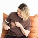 Mum opening the two-way zip on her brown and pink Indiana breastfeeding tee by Milky Threads Co, in a tan leather chair