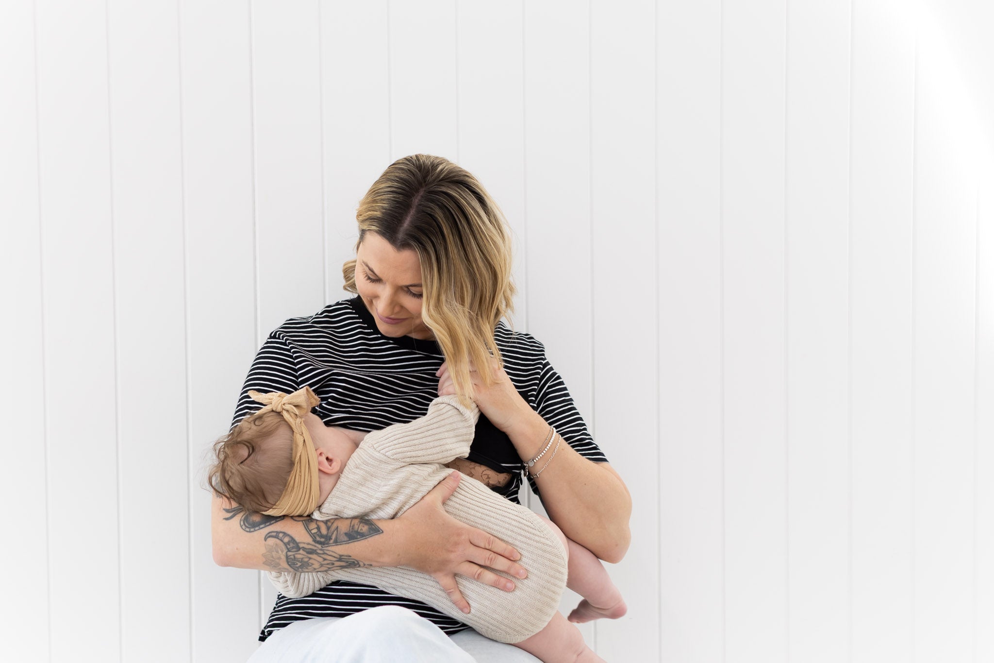 Mum sitting on a chair breastfeeding her baby in the black and white Mackenzie tee