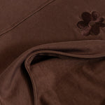 Close-up of the Milky Threads Co flower logo and panel and zip detail on the brown and pink Indiana tee