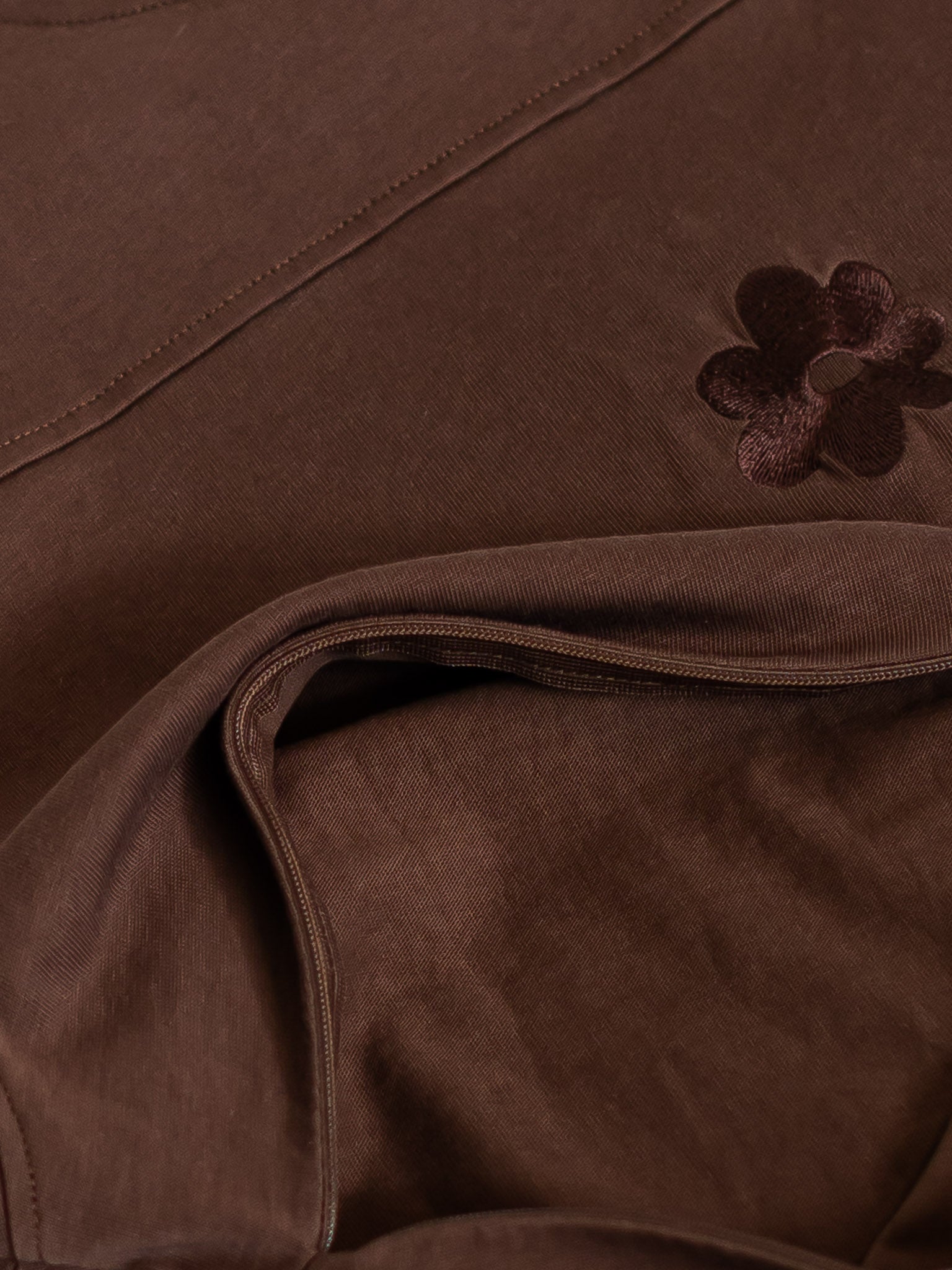 Close-up of the Milky Threads Co flower logo and panel and zip detail on the brown and pink Indiana tee