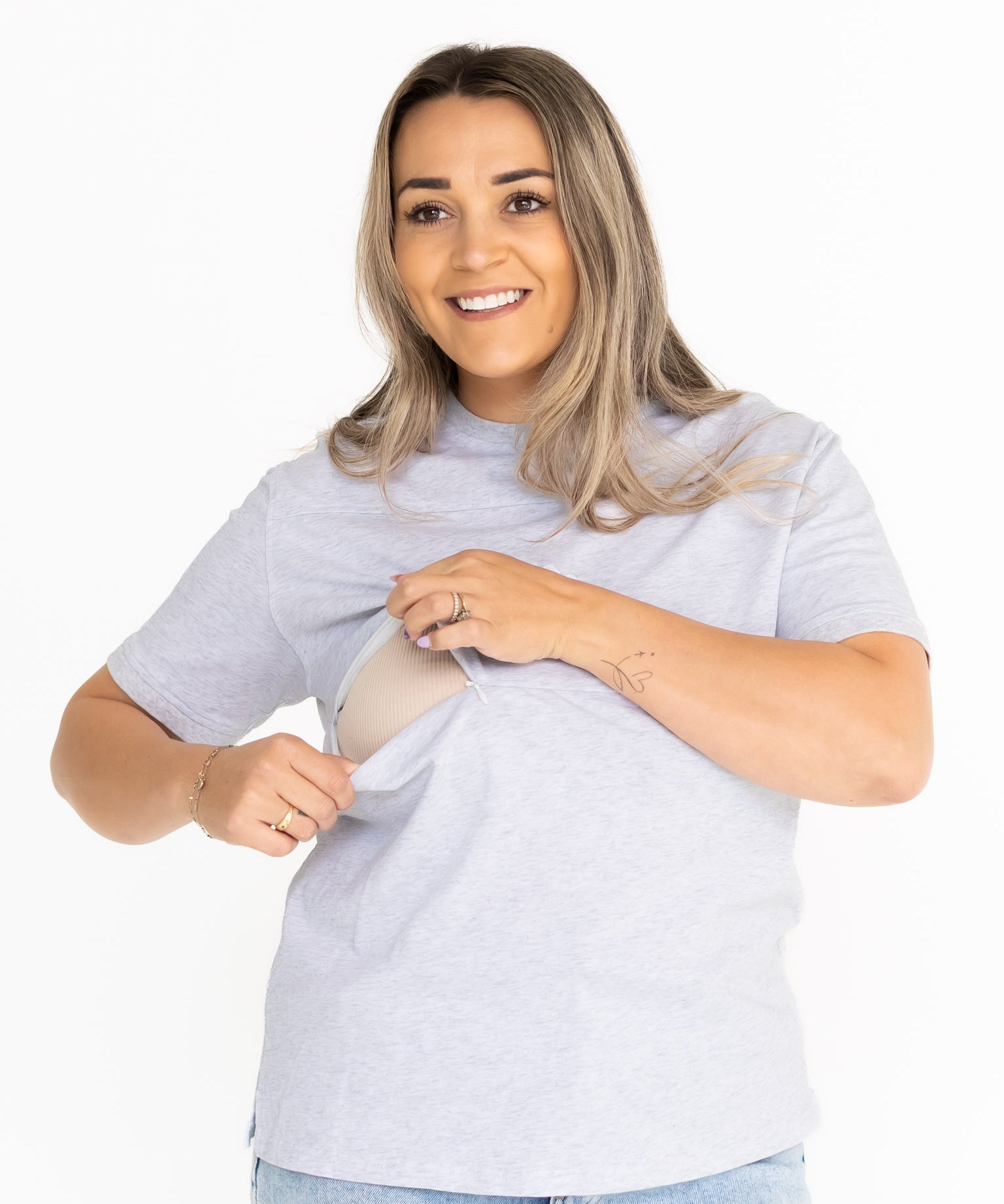 Smiling mum opening the discreet two-way zip on the light grey Indiana breastfeeding tee