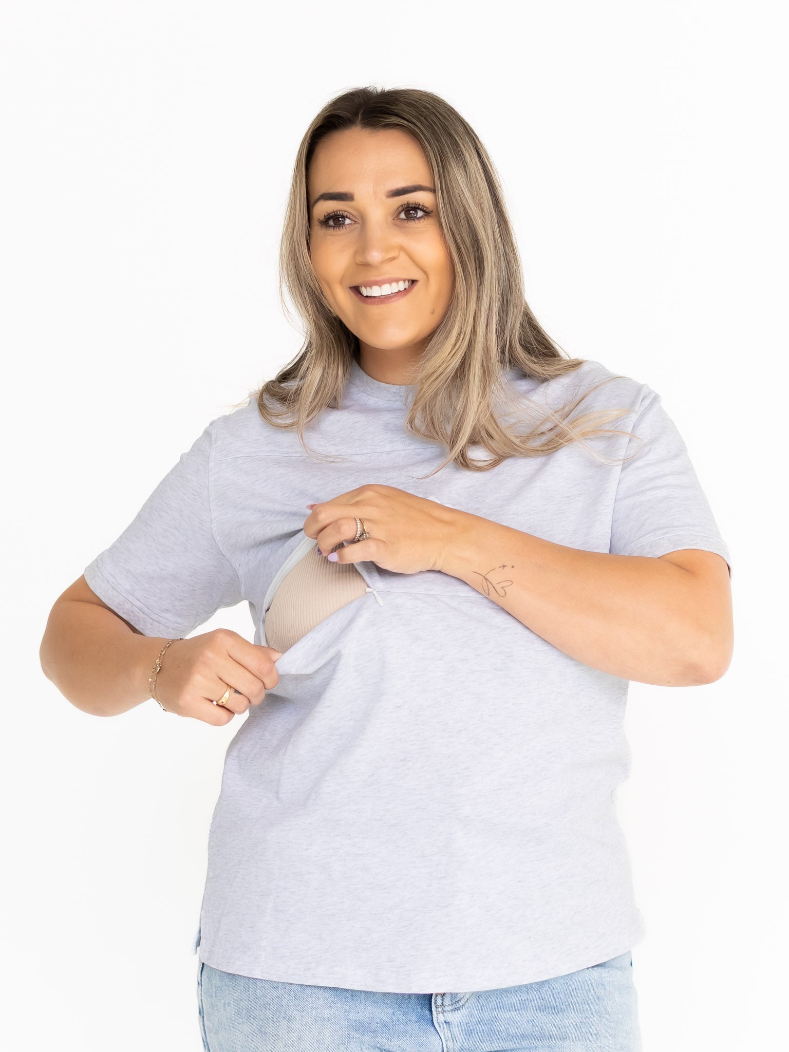 Smiling mum opening the discreet two-way zip on the light grey Indiana breastfeeding tee