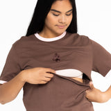 Mum opening the discreet two-way zip on the brown Indiana breastfeeding tee with pink trim
