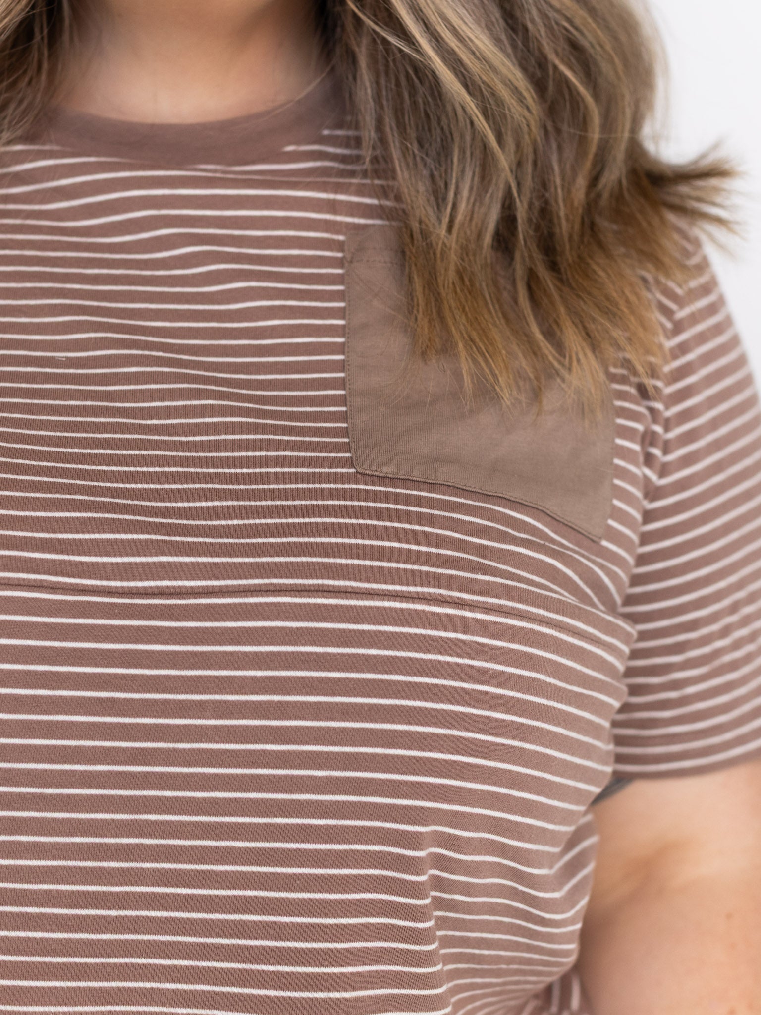 Close-up of the tonal brown chest pocket and zip seam on the brown and white striped Mackenzie tee