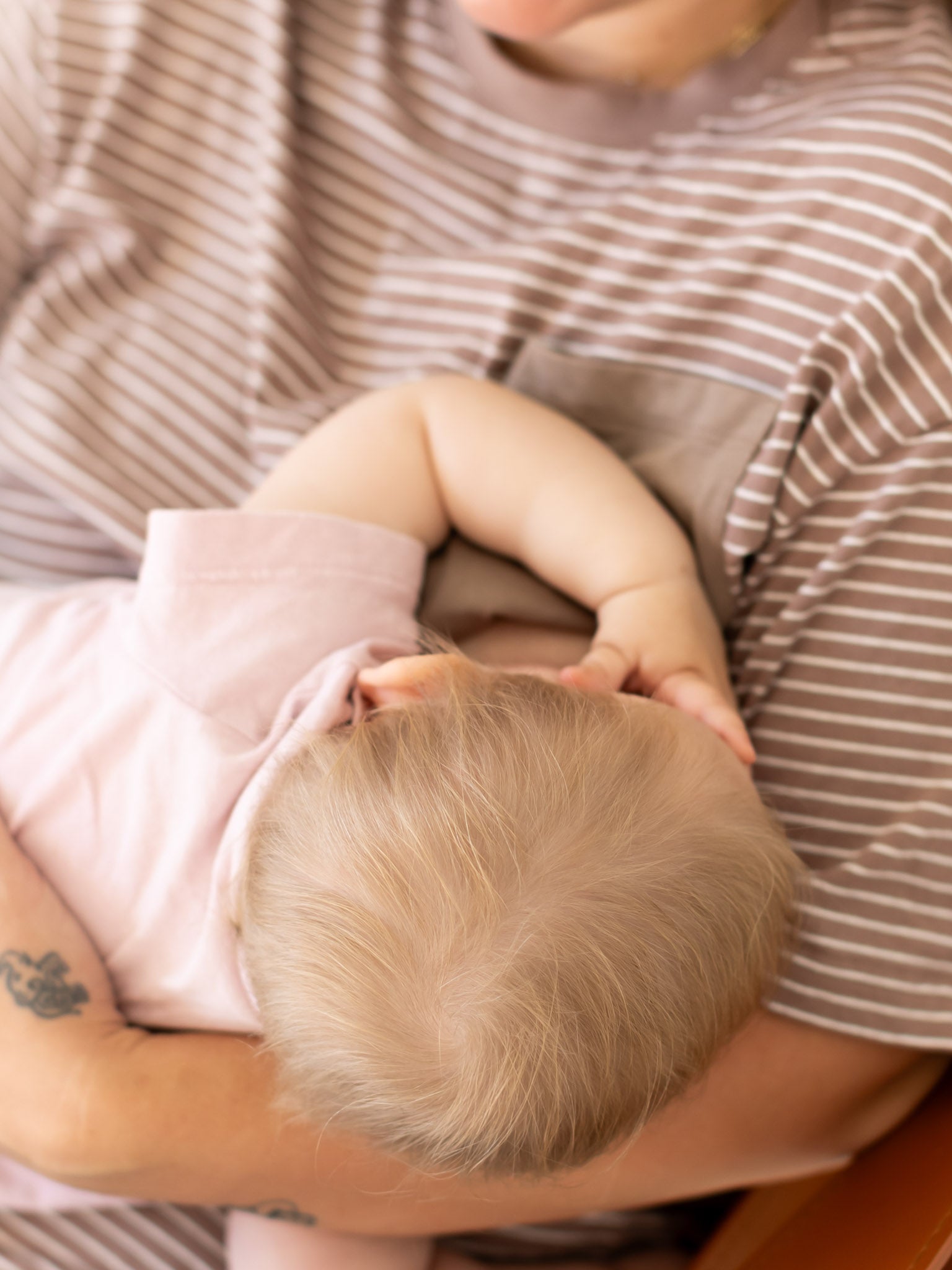 Overhead view of a baby breastfeeding in mum's brown and white striped Mackenzie tee